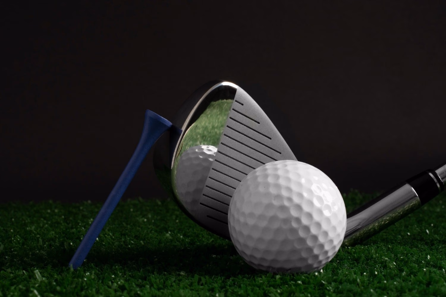 Golf ball beside an iron club and a blue tee on grass