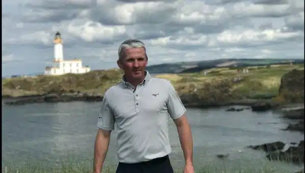 Man standing beside coastal water with a lighthouse in the background