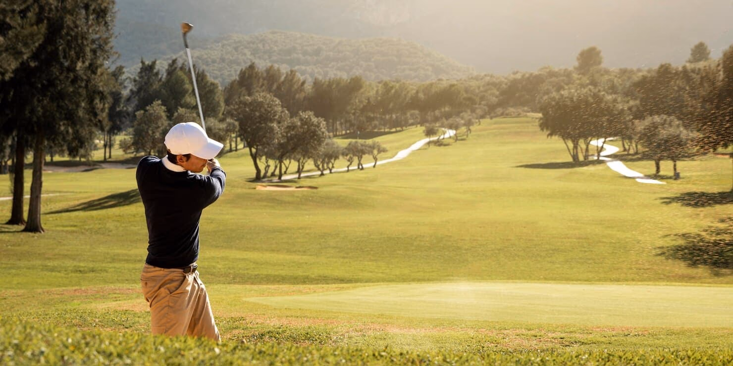 Golfer following through on a swing beside a fairway