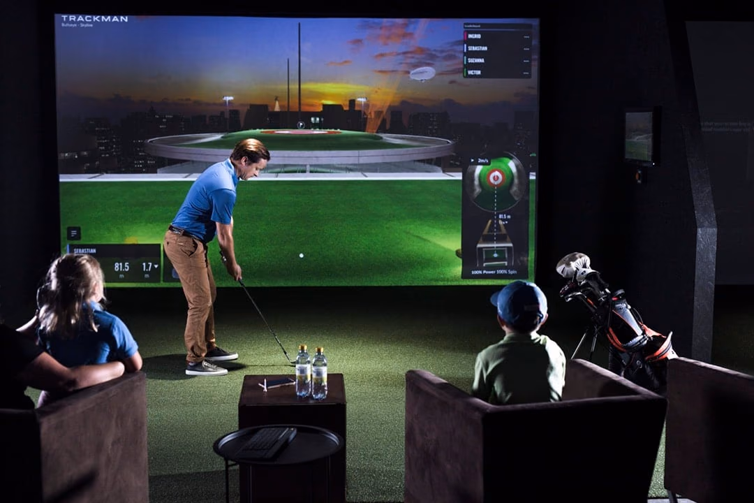 Golfer using an indoor simulator while seated people watch