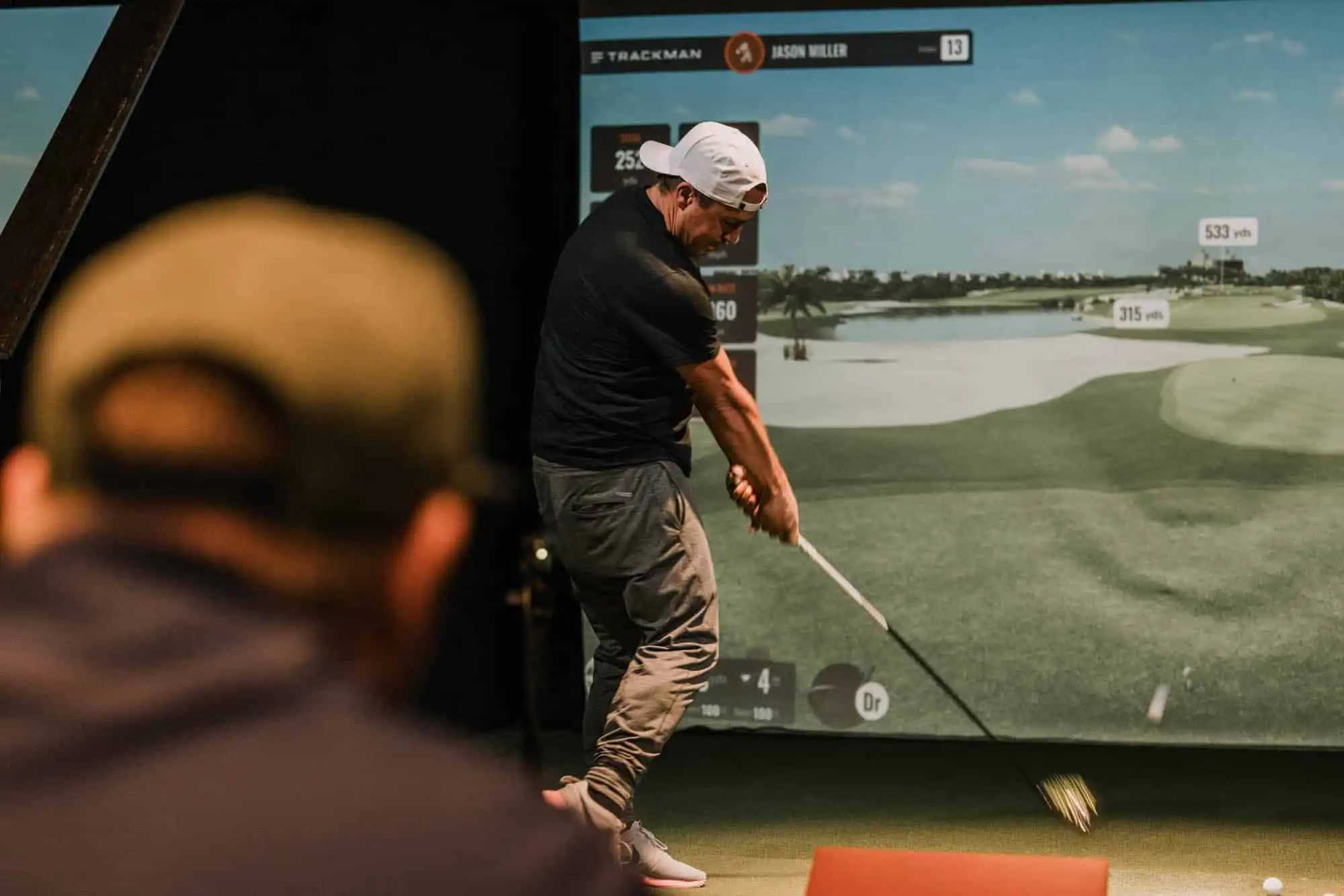 Golfer striking a ball towards an indoor simulator screen