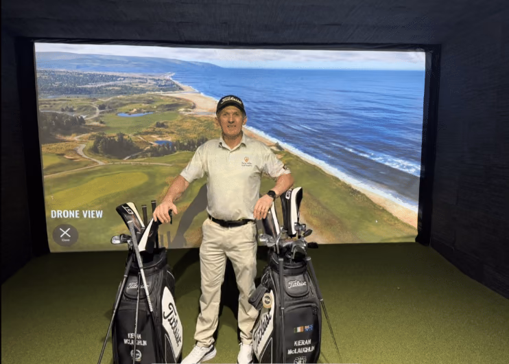 Man standing between golf bags in front of an indoor simulator screen